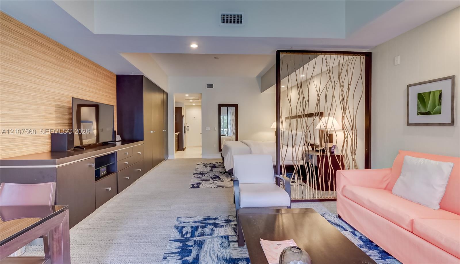 Open-concept interior featuring horizontal wood-slatted accent wall, built-in cabinetry with flat-panel doors, decorative branch-pattern room divider, recessed lighting, and wall-to-wall carpeting