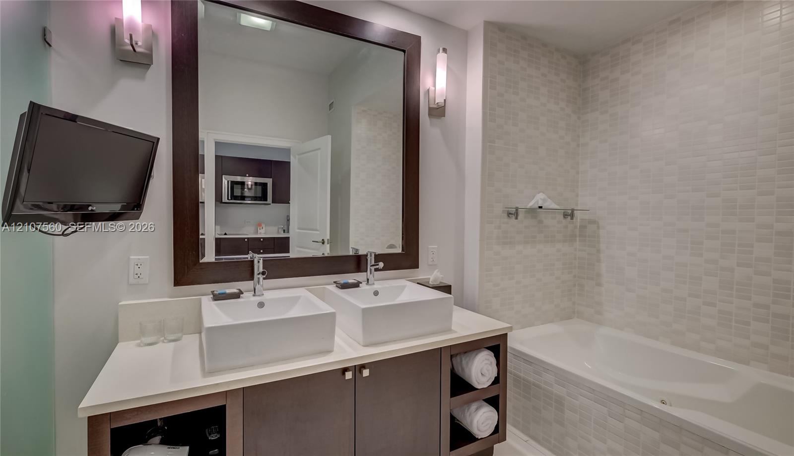 Double vanity featuring square vessel sinks, white countertop, dark-finish cabinetry with open shelving, and a large framed mirror with integrated wall-mounted lighting