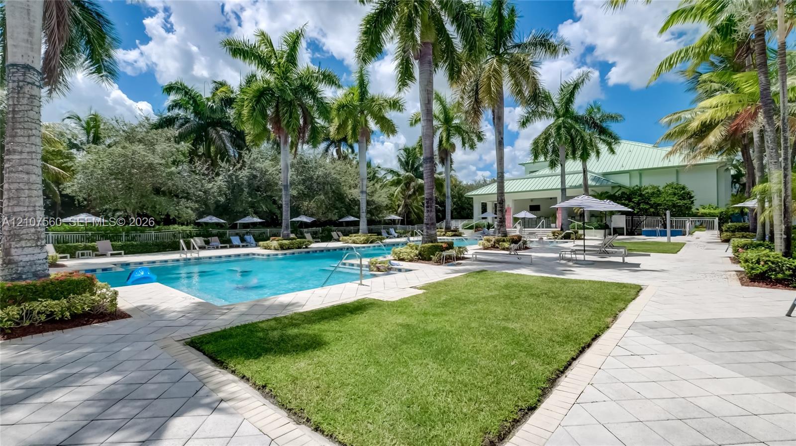 Outdoor swimming pool featuring a paved deck, manicured lawn, palm trees, and structural shaded areas