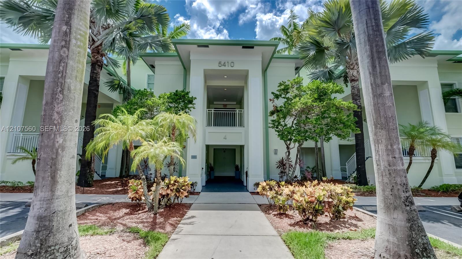 Multi-story exterior featuring a covered entryway, concrete walkway, and mature palm landscaping