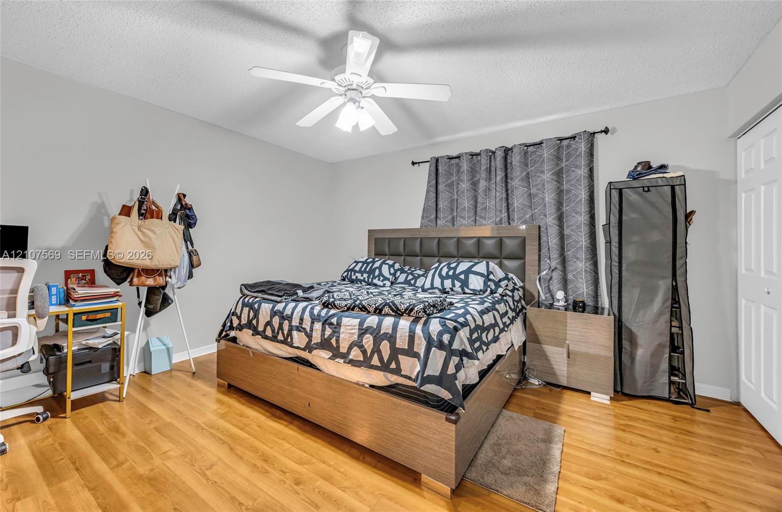 Bedroom featuring wood-finish flooring, a white six-panel closet door, and a white ceiling fan with integrated lighting
