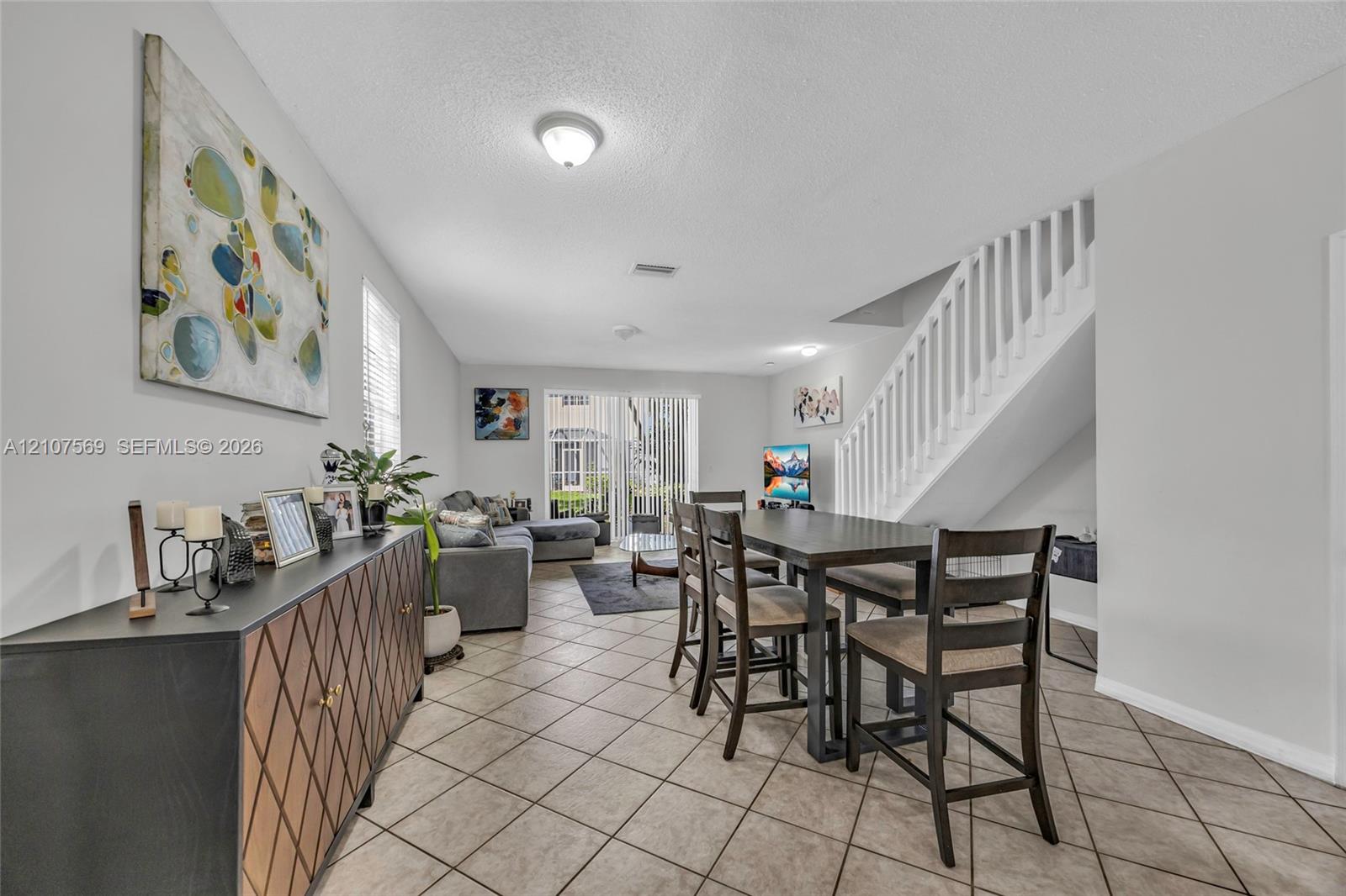 Neutral-toned interior space featuring diagonal-set tile flooring, white-painted staircase with matching balusters, and glass sliding doors providing exterior access