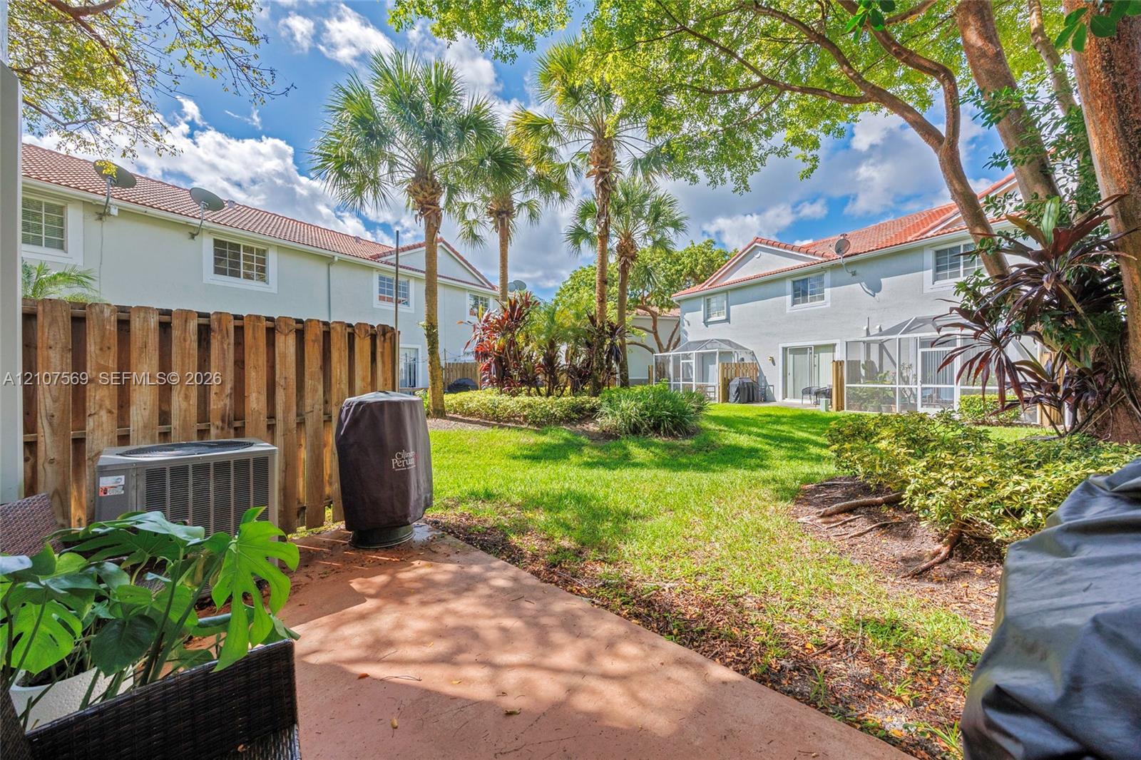 Rear outdoor space featuring a paved patio, wood privacy fencing, mature palm trees, and manicured green space