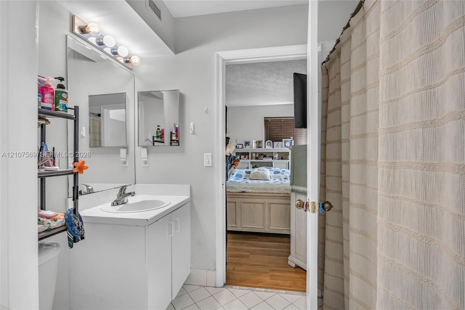 Bathroom featuring a white vanity cabinet, integrated sink with a chrome faucet, large wall-mounted mirror, and tile flooring