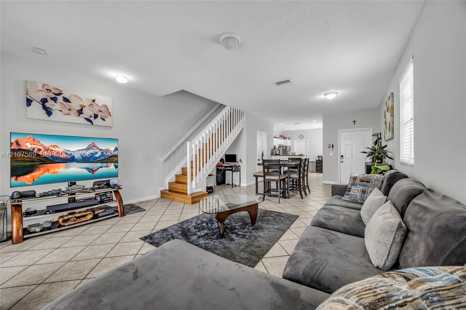 Open concept interior featuring tile flooring, a central staircase with white wood balusters and wood-finish treads, and recessed lighting