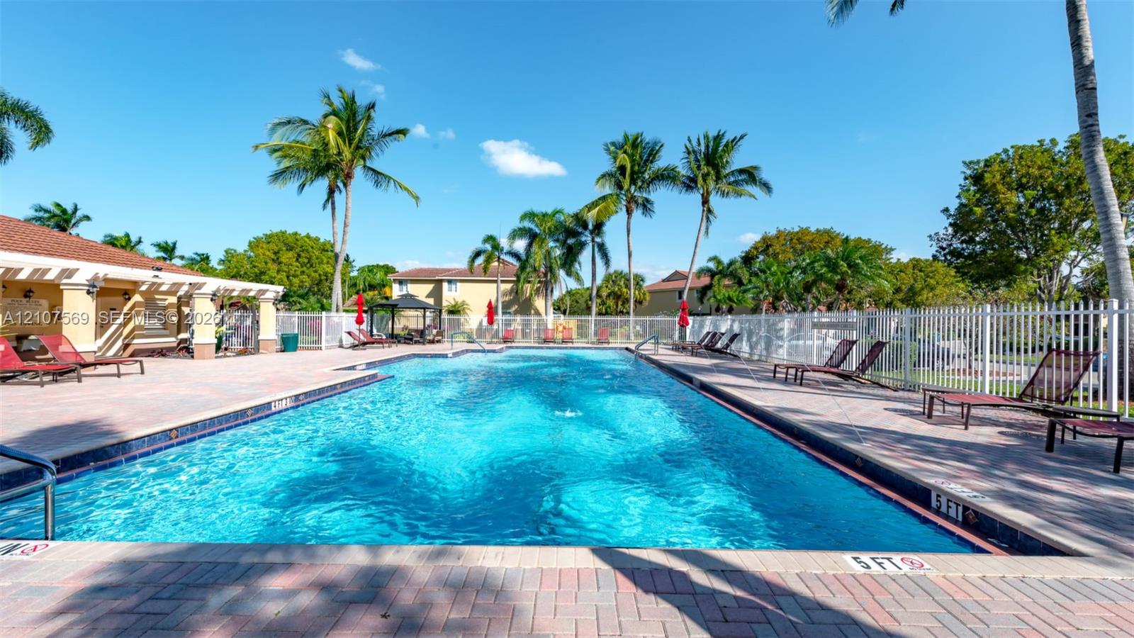 In-ground swimming pool featuring a brick-paver deck, pergola-covered patio, and metal perimeter fencing
