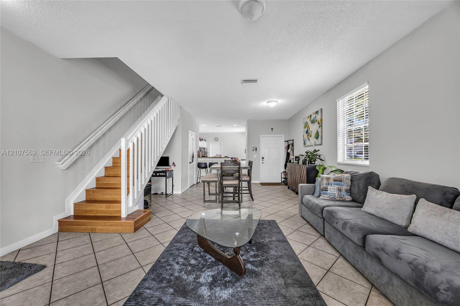 Open-concept interior featuring large-format tile flooring, a staircase with wood treads, and white vertical balusters