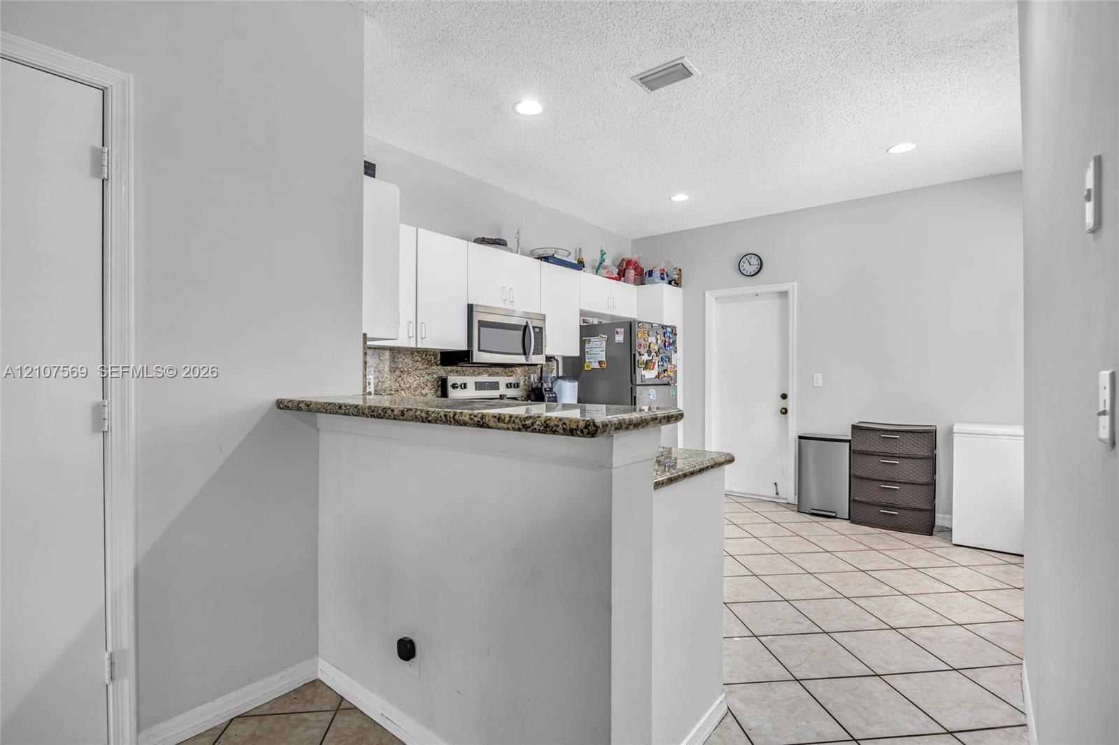 Kitchen featuring white cabinetry, stone-surface countertops, tile flooring, recessed lighting, and a breakfast bar