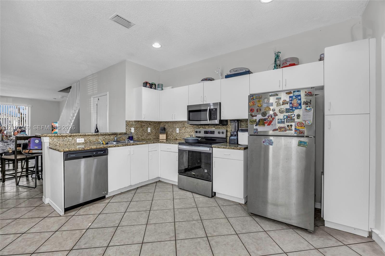 Kitchen featuring white shaker-style cabinetry, stone countertops, stainless steel appliances, and ceramic tile flooring