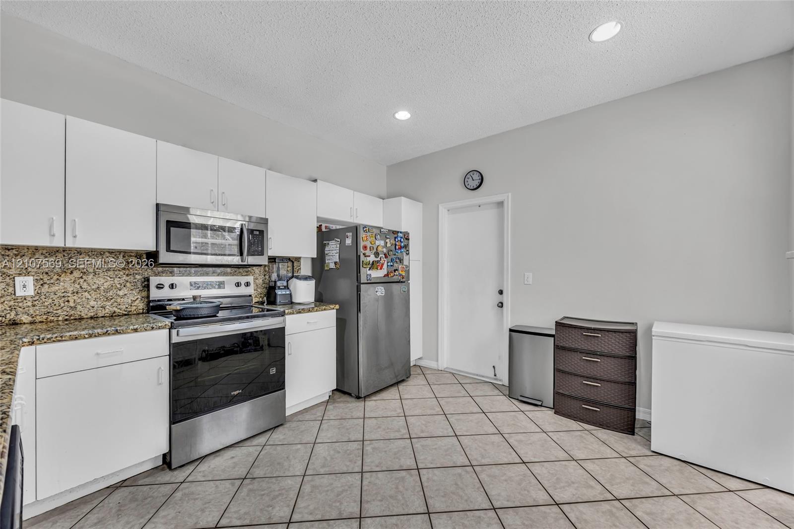 Kitchen featuring white cabinetry, stone countertops, stainless steel appliances, and ceramic tile flooring