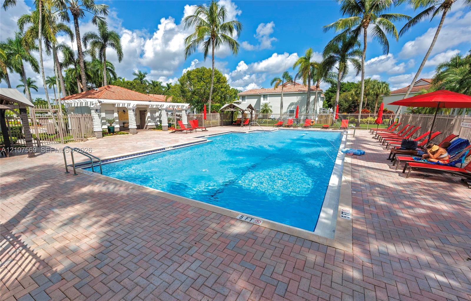 Rectangular swimming pool featuring brick paver decking, a covered poolside pavilion, and mature palm trees