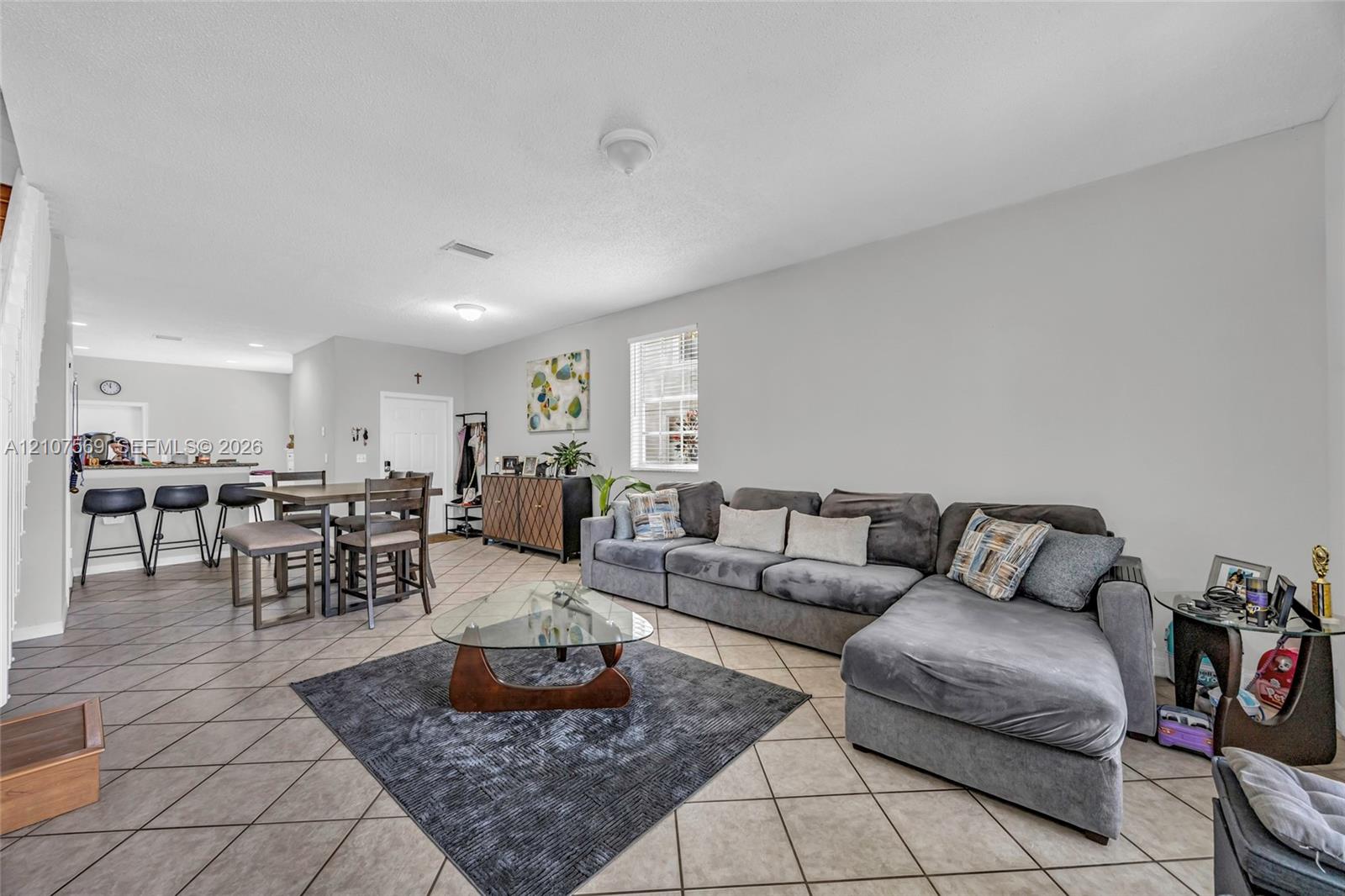 Open-concept interior featuring neutral wall tones, large-format tile flooring laid on the diagonal, and a breakfast bar