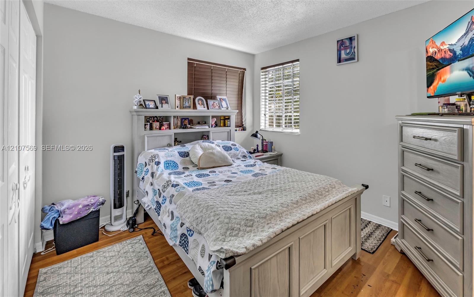 Neutral walls, wood-finish flooring, dual windows with horizontal blinds, and paneled closet doors