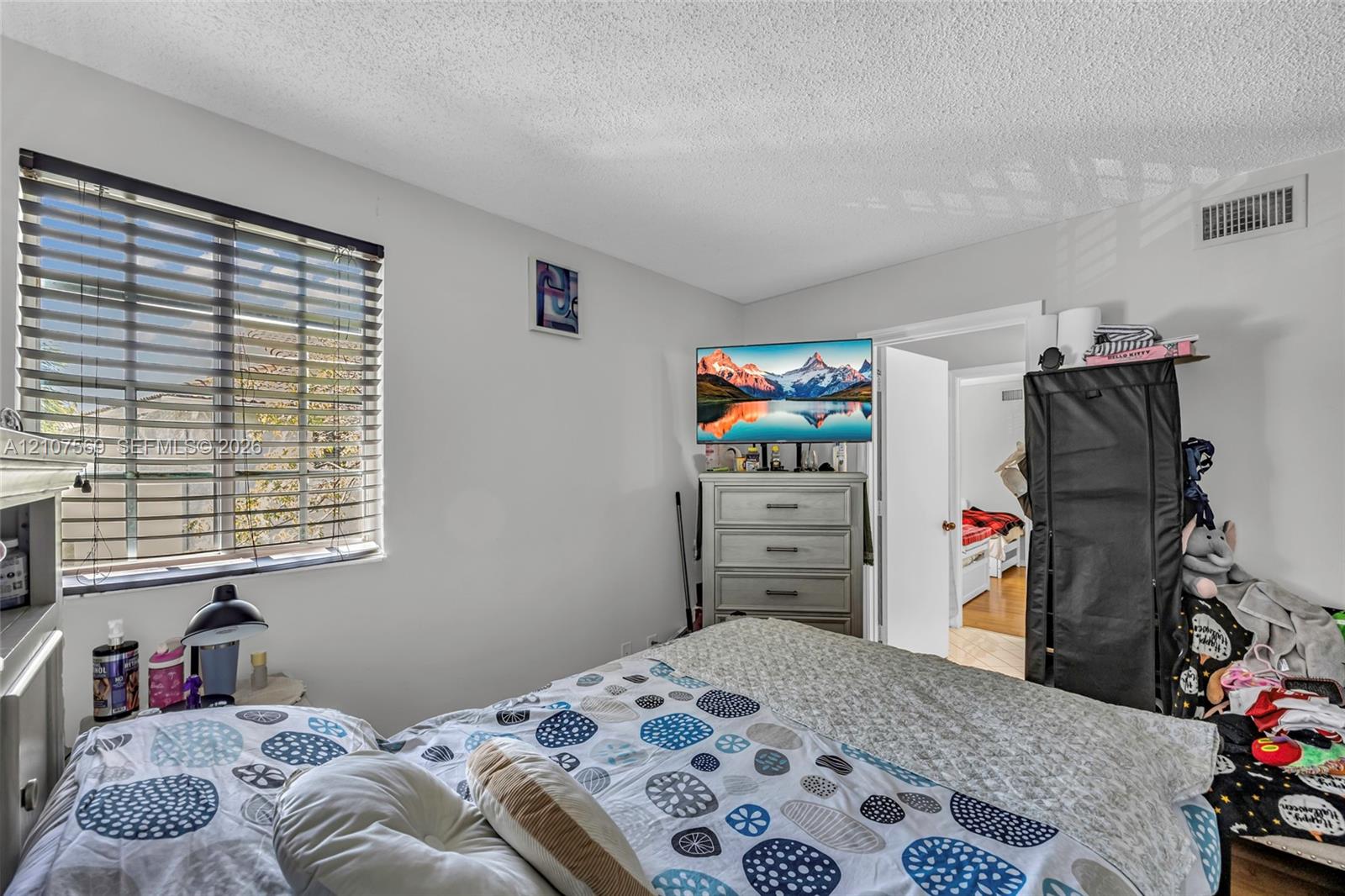 Bedroom featuring horizontal window blinds, textured ceiling finish, and interior door with brushed metal hardware
