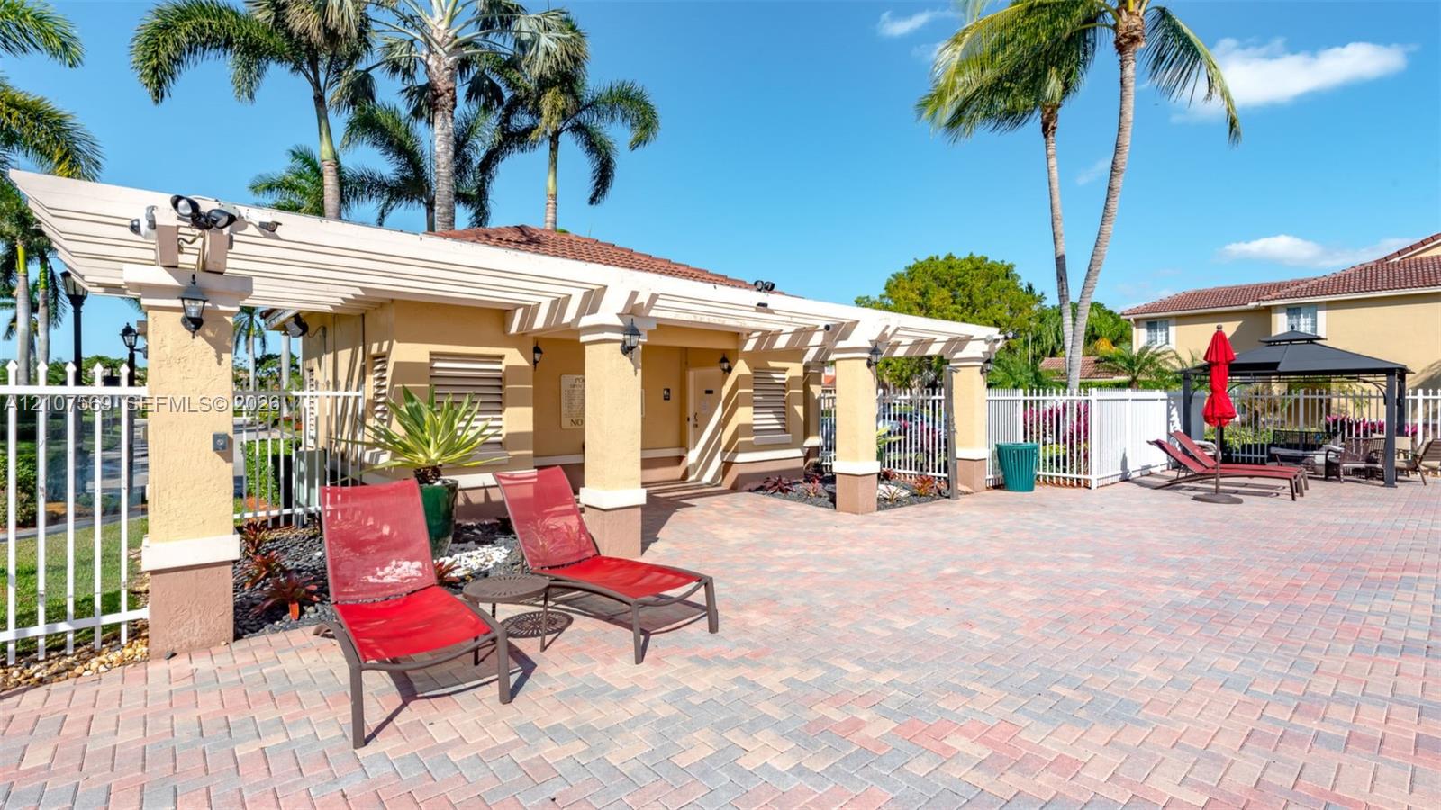 Outdoor pavilion featuring a white pergola, textured stucco columns, paver patio, and white metal fencing