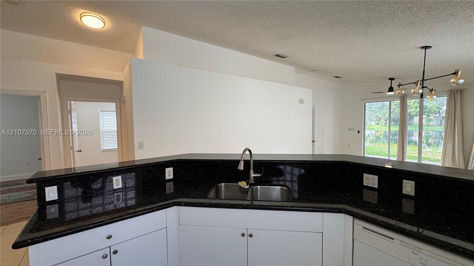 Kitchen featuring a wraparound dark stone countertop, double-basin undermount sink with a gooseneck faucet, white cabinetry, and a multi-arm chandelier