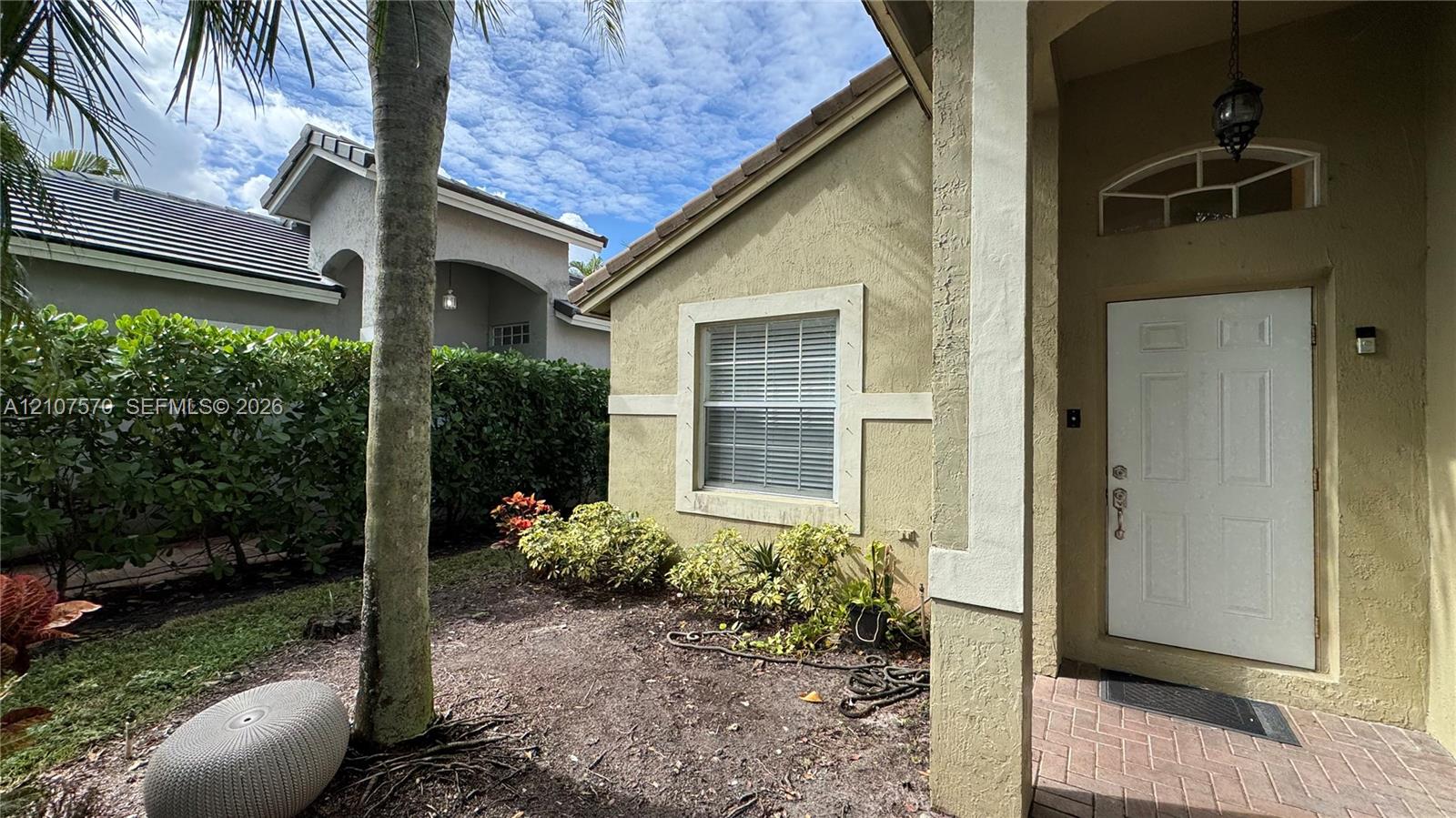 Stucco exterior featuring a covered entryway with a brick-paver porch, transom window, and tiled roof