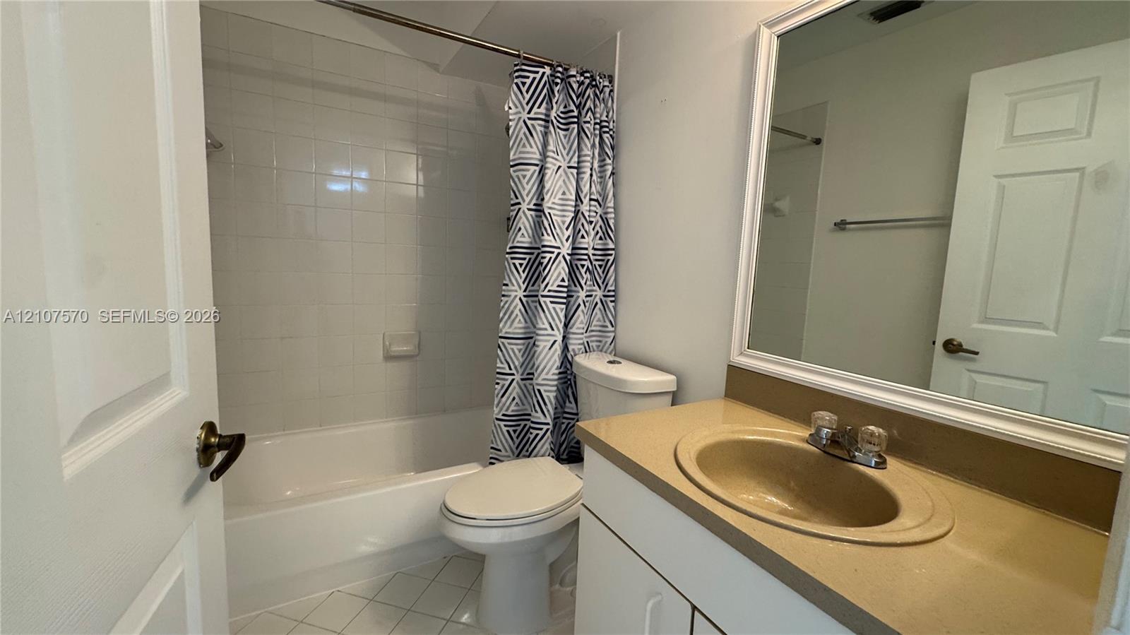 Bathroom featuring a vanity with a solid-surface integrated sink, a full-width mirror, tile flooring, and a shower-tub combination with a tiled surround