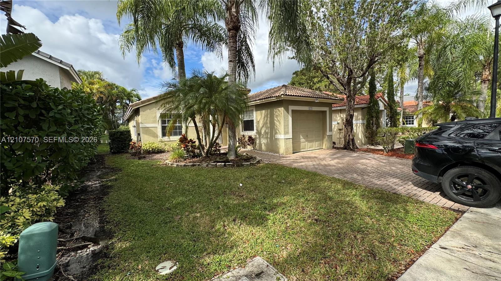 Stucco exterior residence featuring a tile roof, single-car garage, and a paver driveway, complemented by mature landscaping