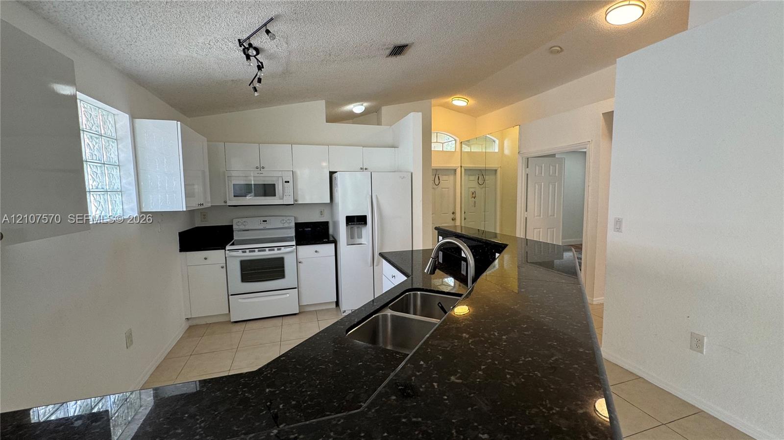 Kitchen featuring white cabinetry, dark stone-finish countertops, ceramic tile flooring, a dual-basin stainless steel sink with a high-arch faucet, and glass block accent windows