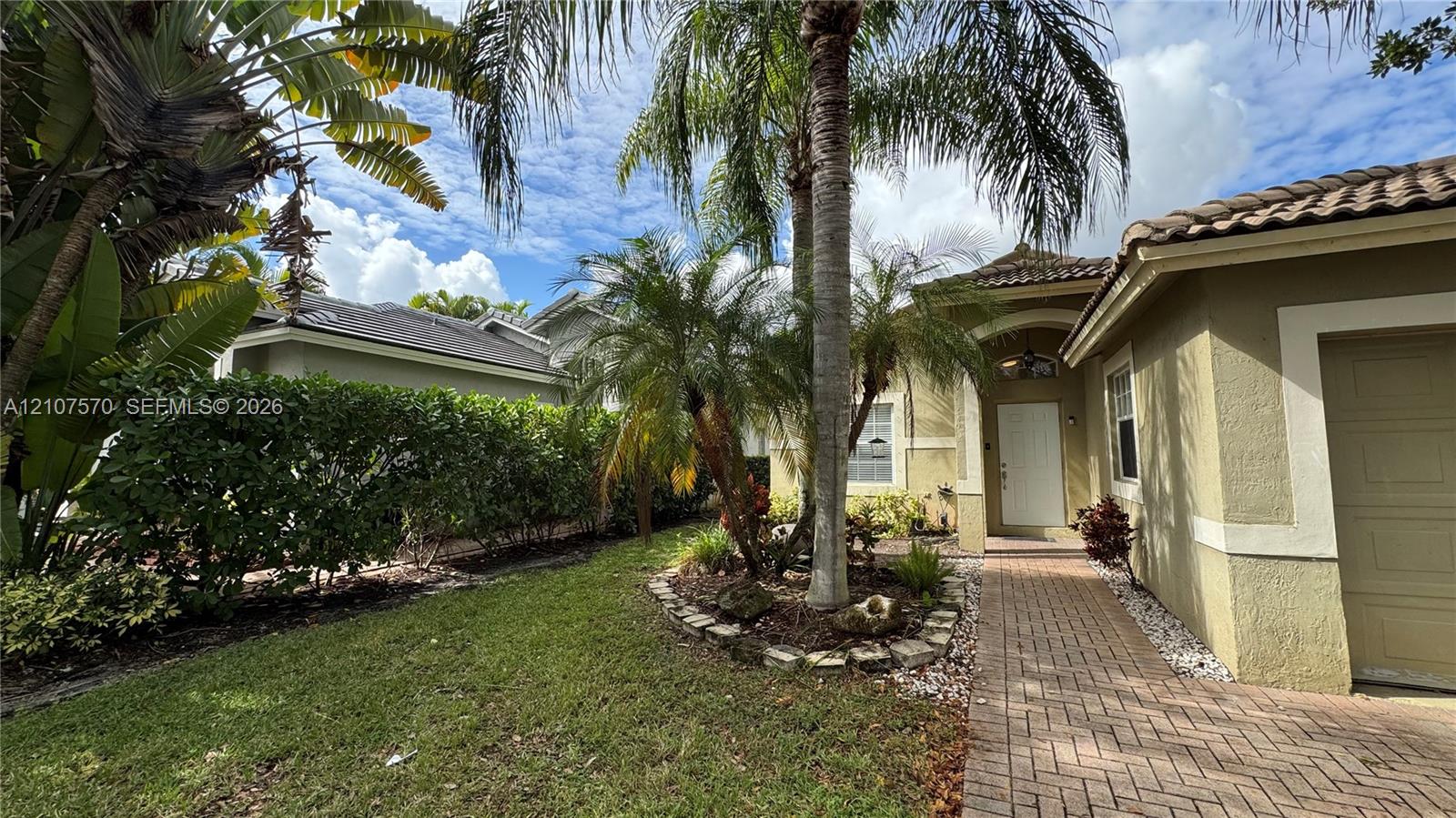 Exterior facade featuring a stucco finish, arched entryway, brick-paver walkway, tile roof, and mature palm landscaping