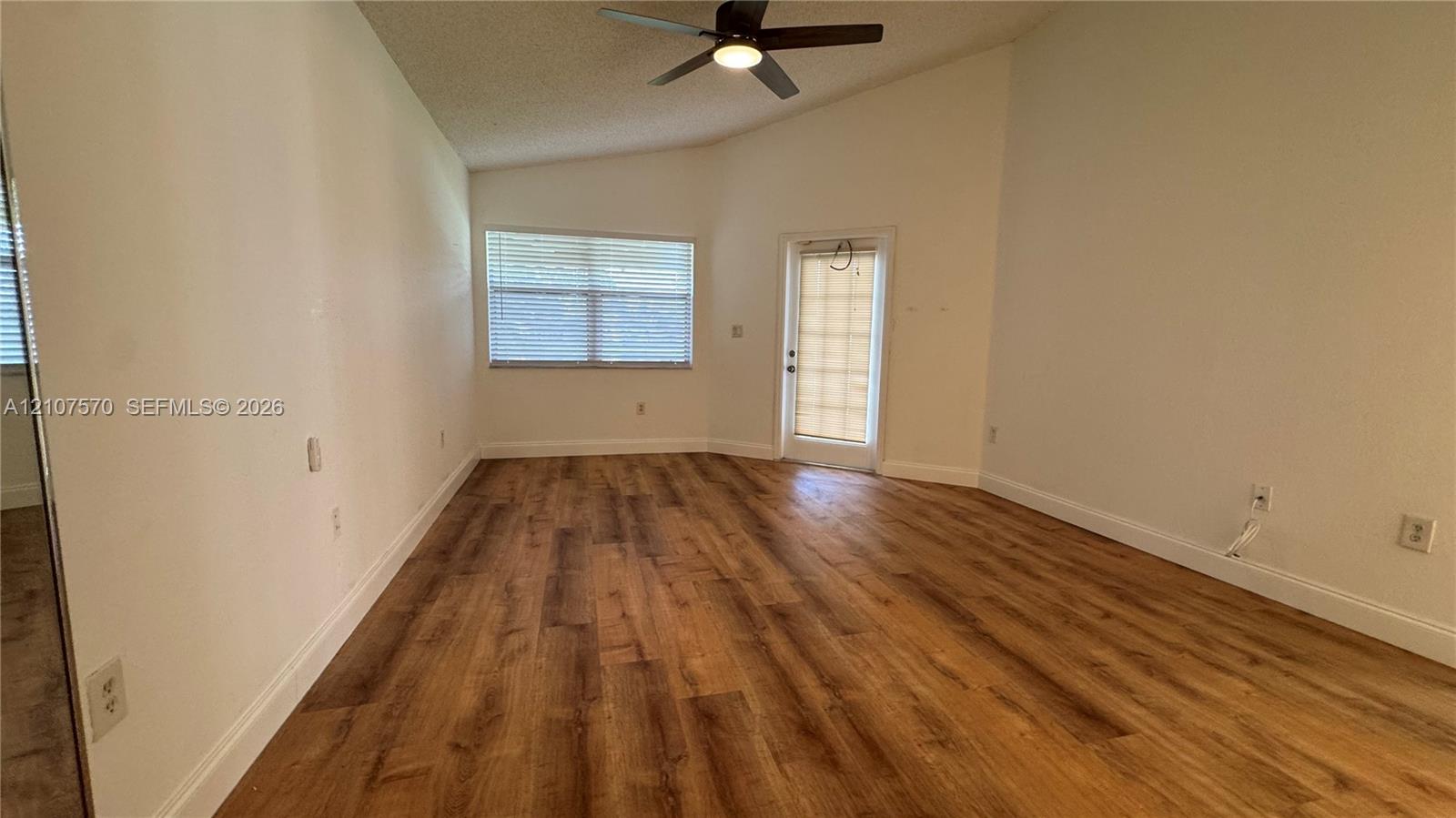 Vaulted ceilings featuring a central overhead fan, wood-finish flooring, and natural light provided by a window and glass-panel door