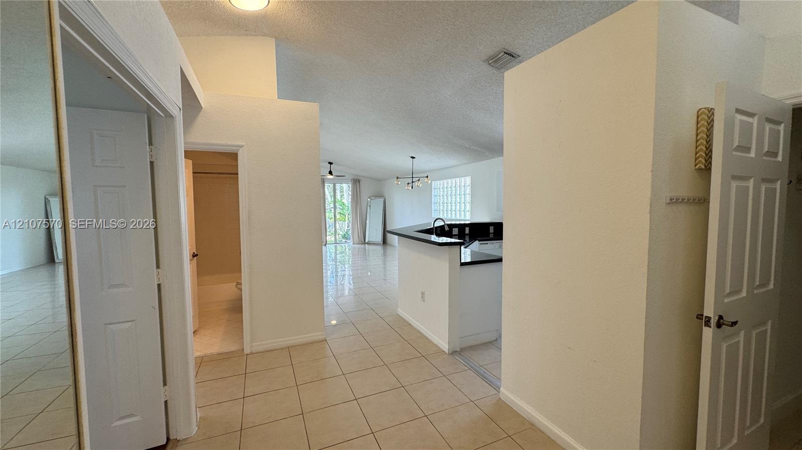 Interior featuring vaulted ceilings, neutral ceramic tile flooring, kitchen peninsula with dark stone countertop, glass block wall accent, and six-panel interior doors