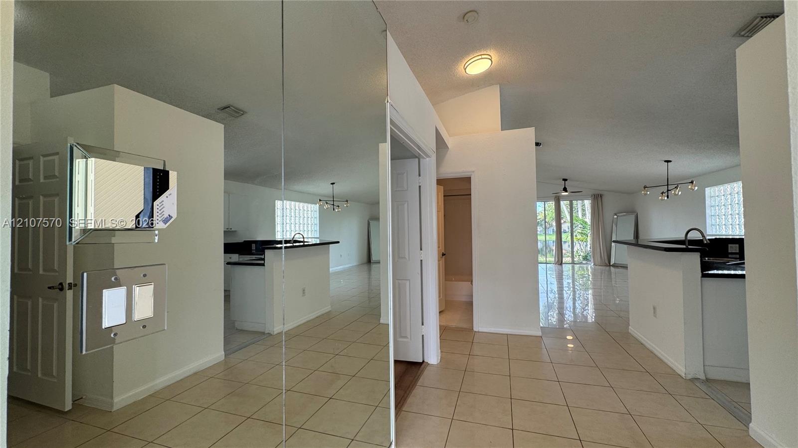Full-height wall mirrors, neutral ceramic tile flooring, vaulted ceilings, glass block window accents, and recessed and pendant lighting