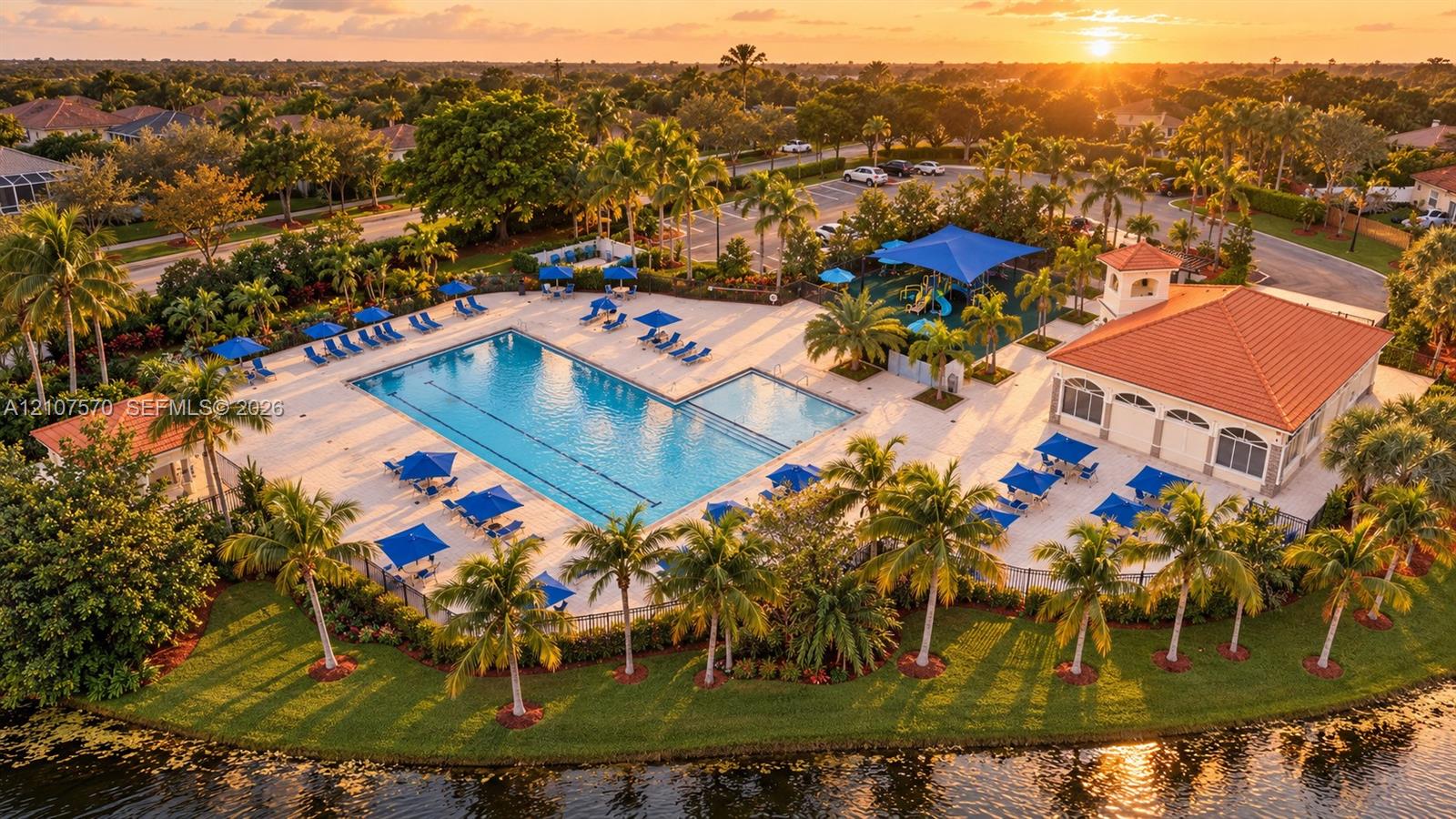 Community recreation center featuring a swimming pool, covered clubhouse with a tiled roof, playground, and paved deck area situated on a waterfront lot