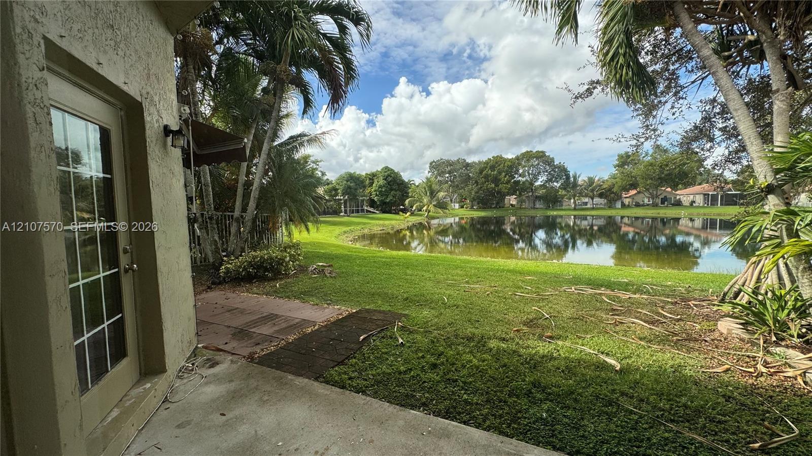 Waterfront backyard featuring a concrete patio, grassy lawn, and mature palm trees