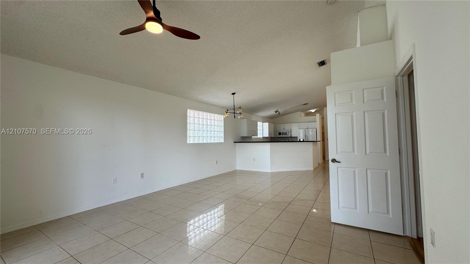 Open-concept interior featuring large-format tile flooring, vaulted ceilings, a structural glass block window, and a ceiling fan with integrated lighting
