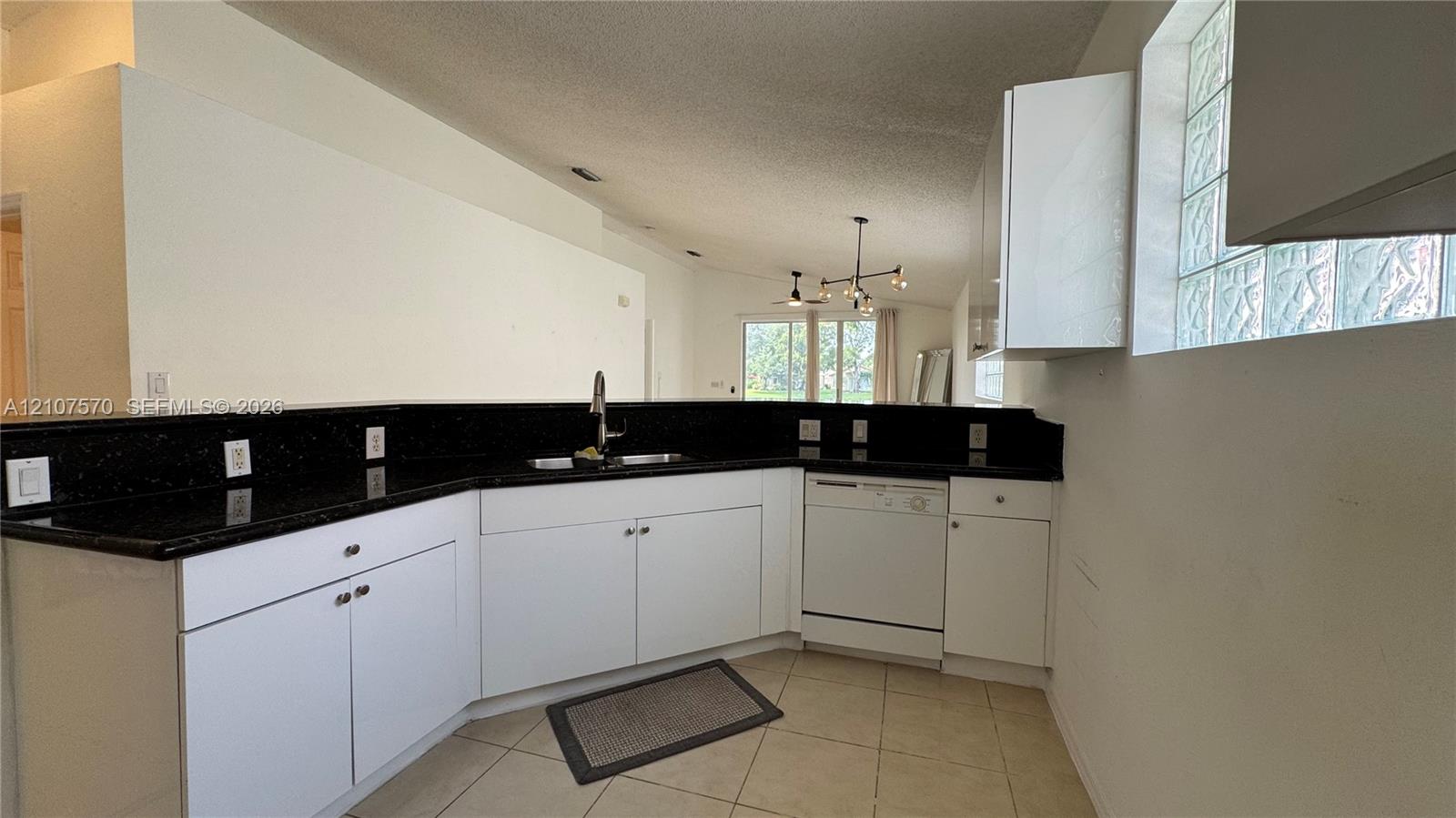 Kitchen featuring white cabinetry, dark stone countertops, stainless steel undermount sink, integrated dishwasher, and glass block window detailing