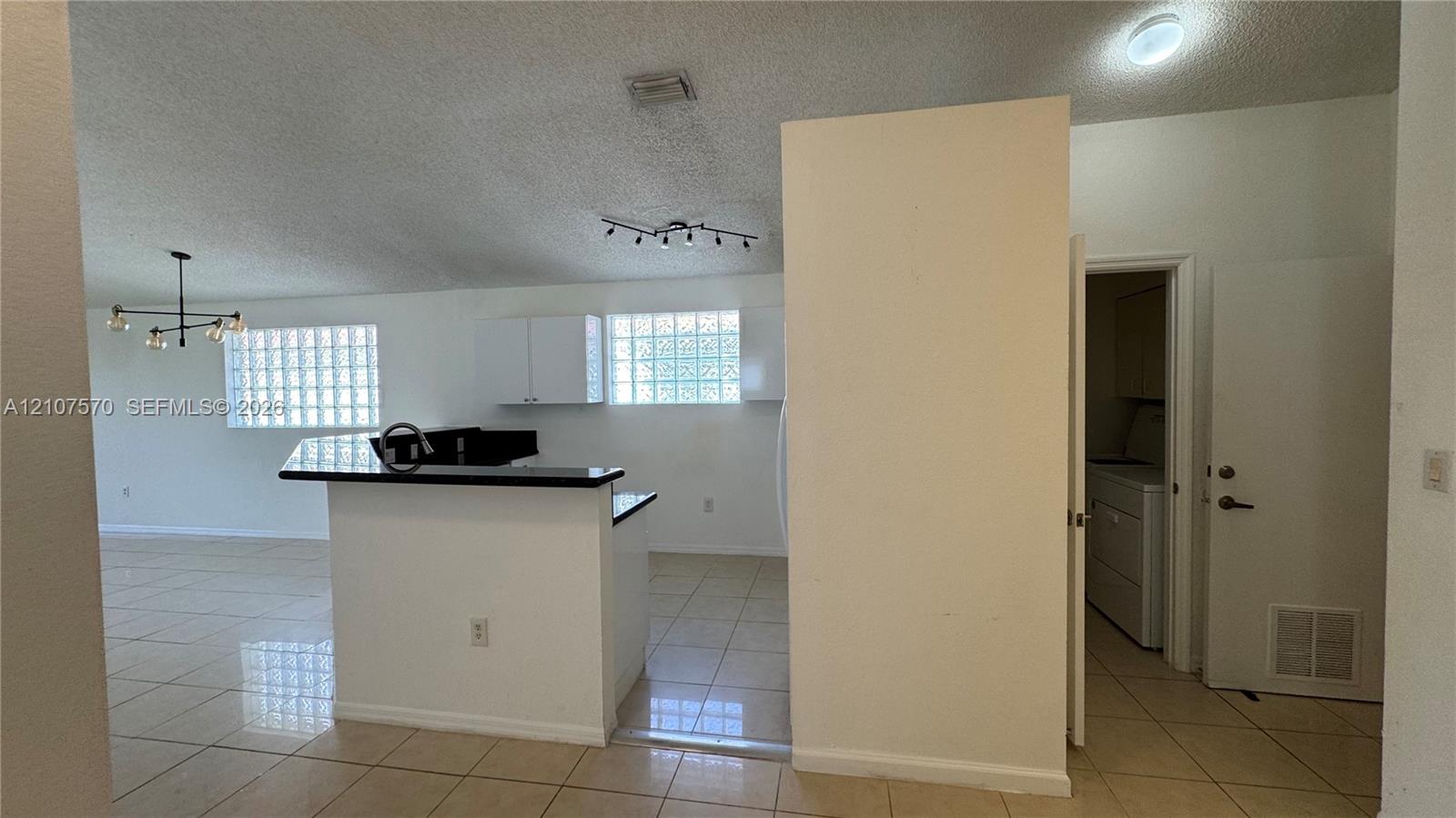 Kitchen featuring a raised breakfast bar with dark solid-surface countertops, white cabinetry, glass block windows, and ceramic tile flooring