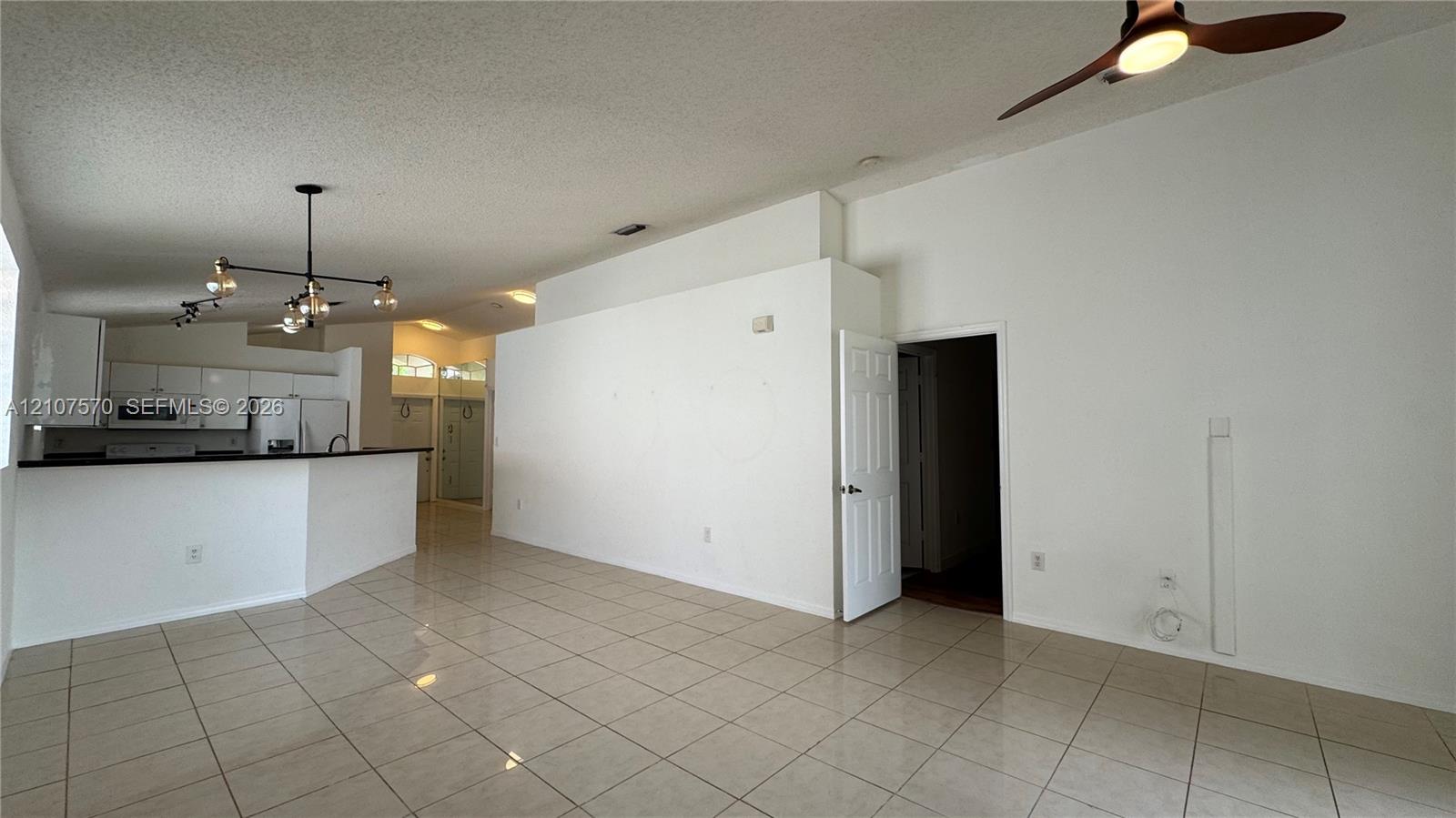 Open-concept area featuring light-toned tile flooring, vaulted ceilings, a multi-arm modern light fixture, and a built-in kitchen breakfast bar