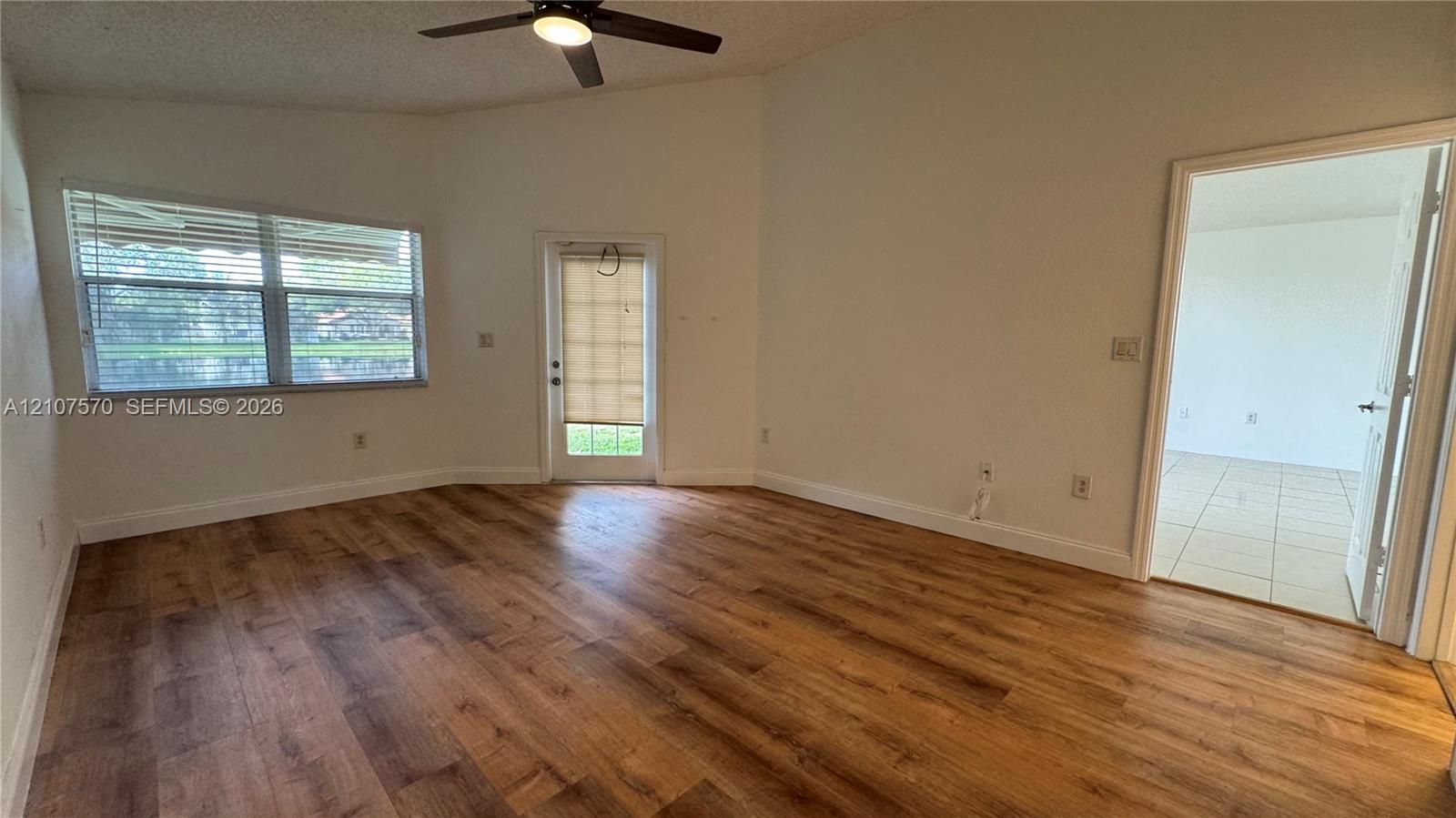 Vaulted ceiling with a central integrated light fixture and ceiling fan, wood-finish flooring, and natural light from a dual-pane window and a glass-paneled door