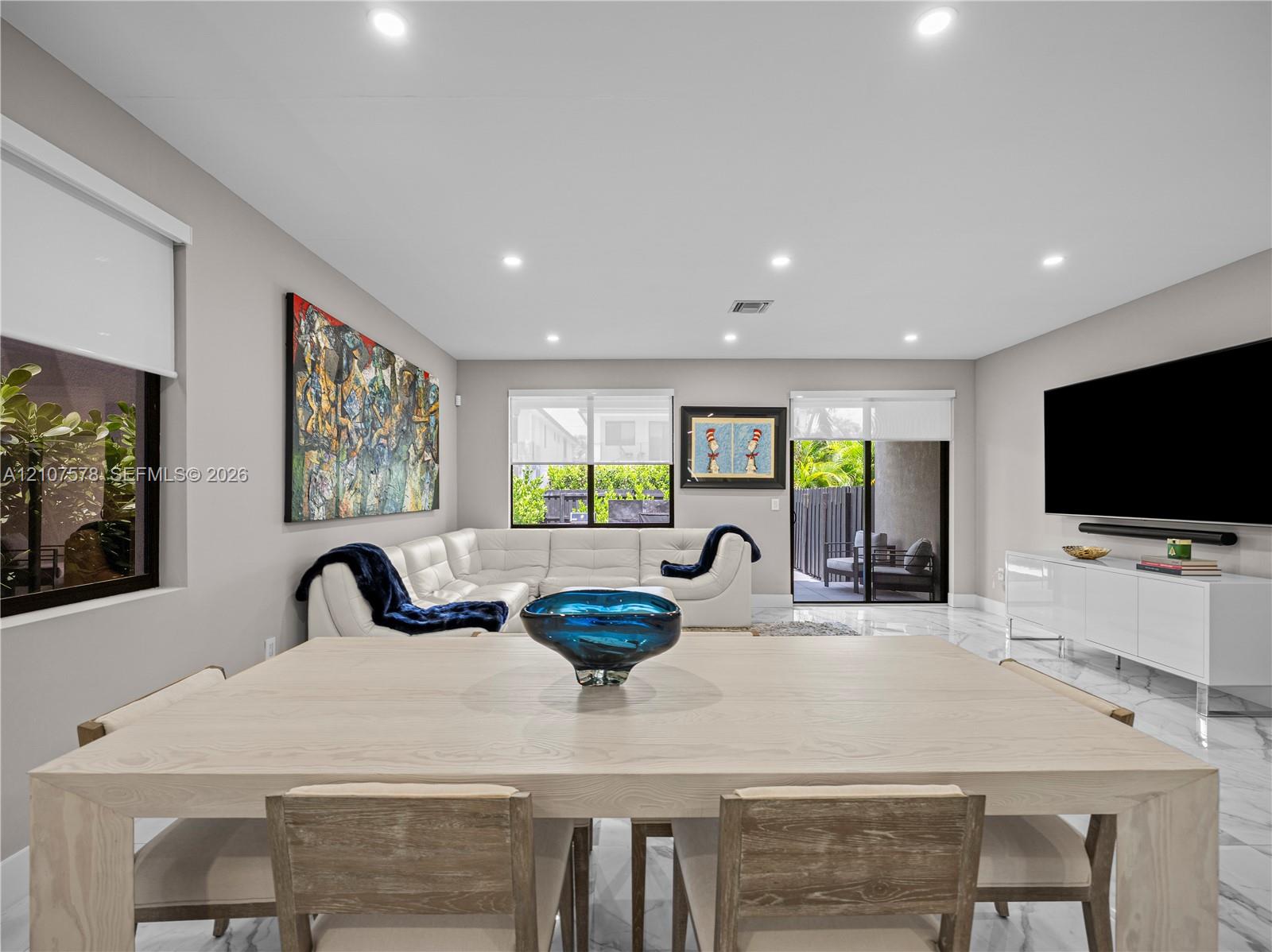 Open-concept living space featuring large-format tile flooring, recessed lighting, multiple windows with roller shades, and a sliding glass door
