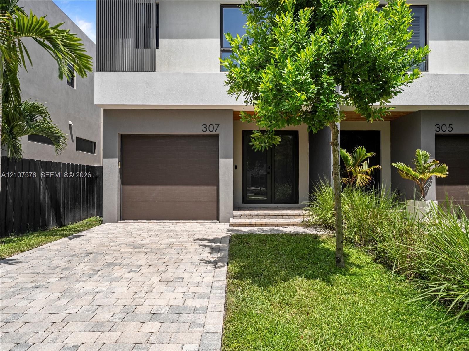 Modern two-story exterior featuring a paver driveway, an attached garage, glass-paneled entry doors, and professional landscaping