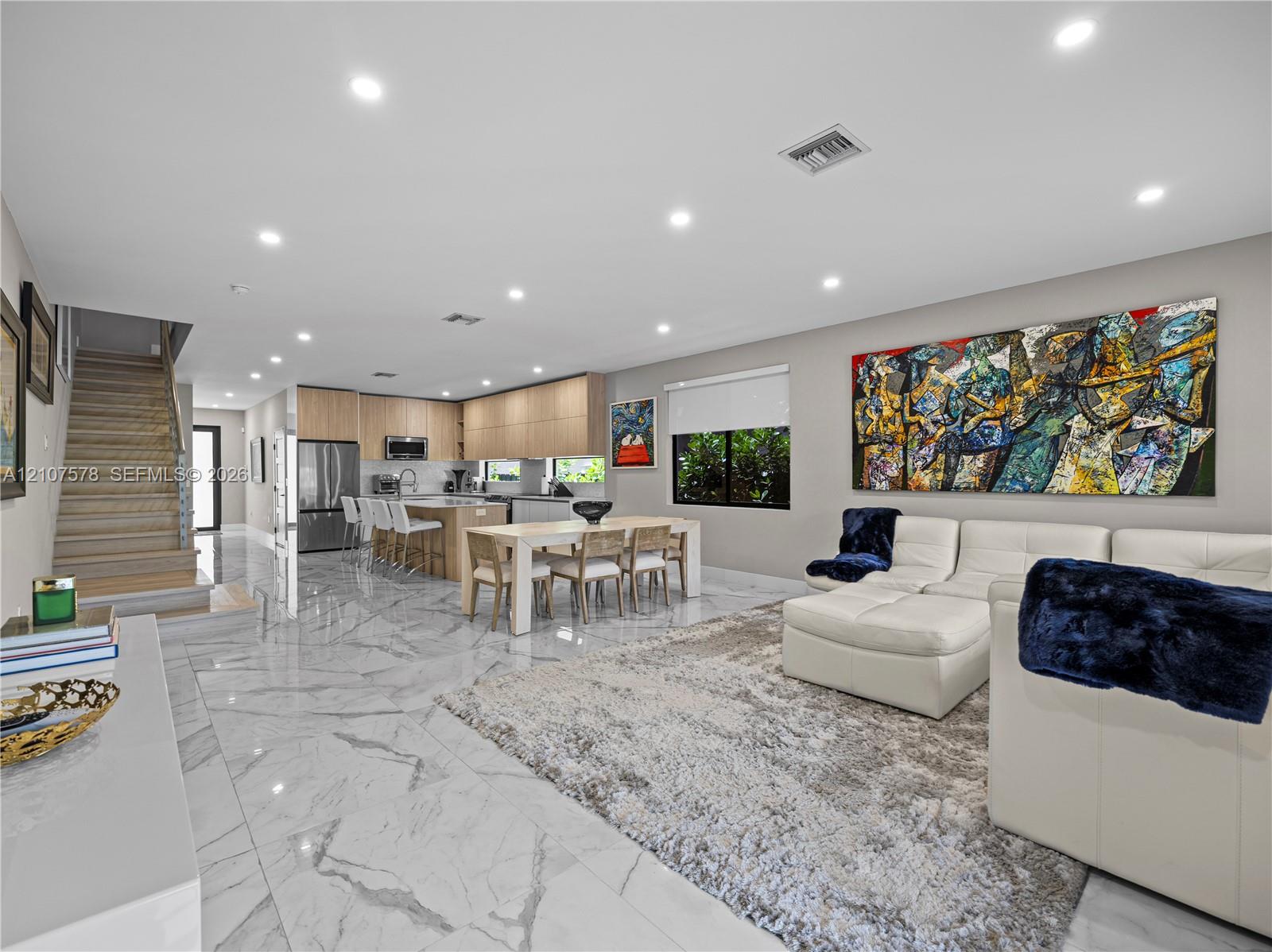 Open concept floor plan featuring stone-finish flooring, recessed lighting, a kitchen with flat-panel cabinetry, and a tiered staircase