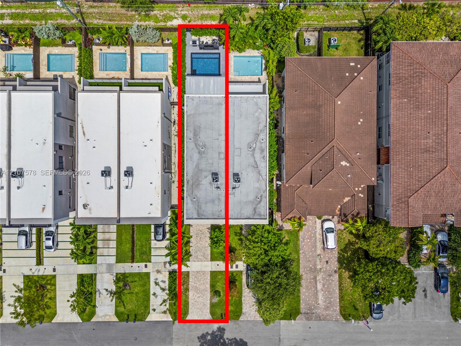 Aerial perspective featuring a paved driveway, a flat roofline, and a rear swimming pool with a stone-surfaced patio