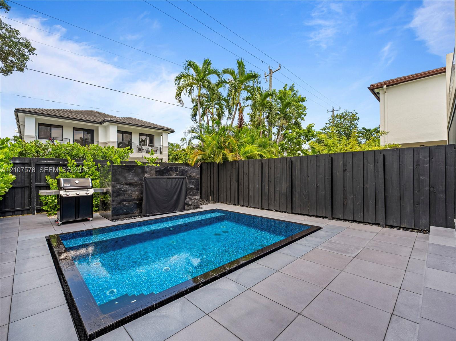 In-ground swimming pool with tiled surround, stone-clad water feature, and dark wood privacy fencing