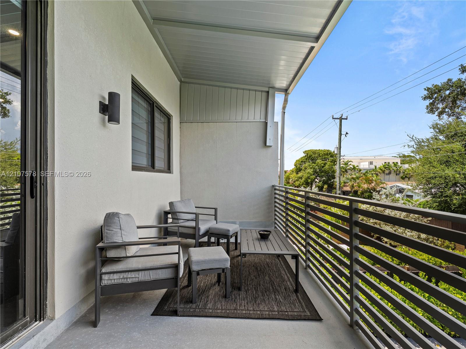 Covered balcony featuring a horizontal metal railing, smooth stucco exterior walls, and wall-mounted exterior cylinder lighting