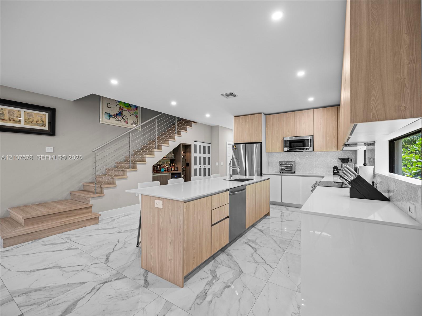 Kitchen featuring light wood-finish cabinetry, white stone countertops, stainless steel appliances, and large-format porcelain tile flooring
