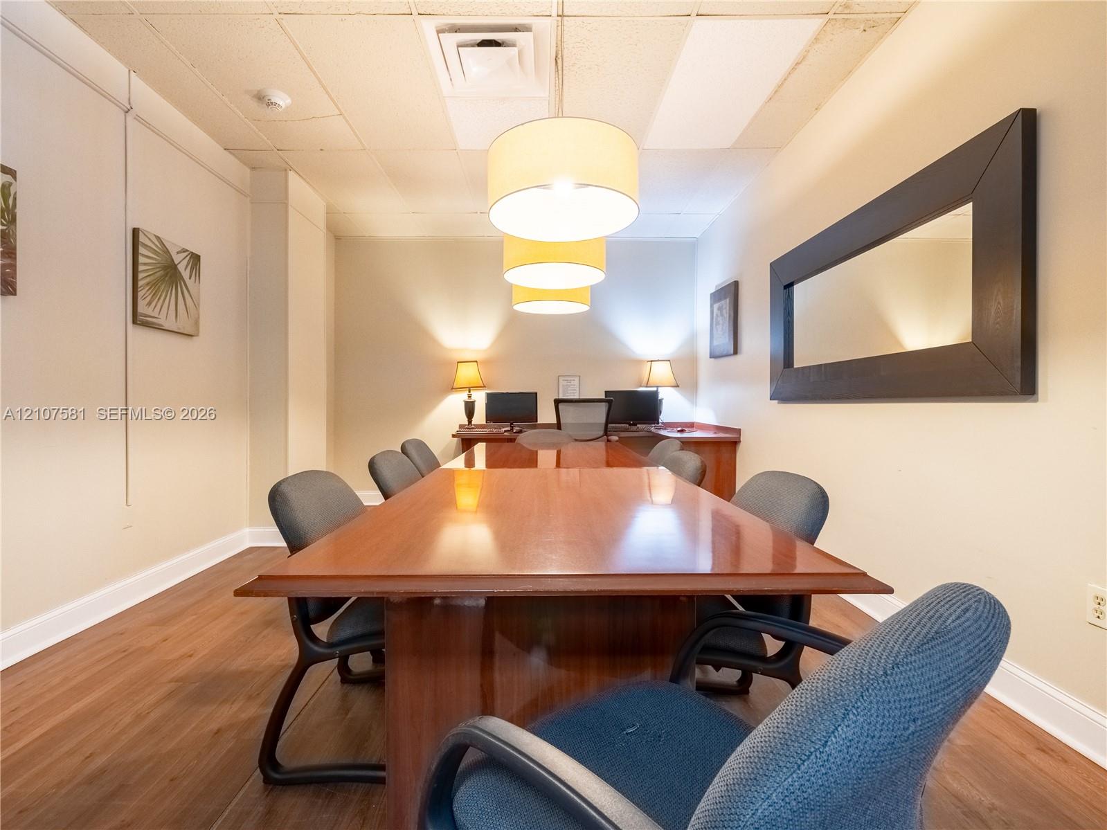 Wood-finish flooring with white baseboards, suspended ceiling with recessed lighting, and a large rectangular mirror with a dark frame