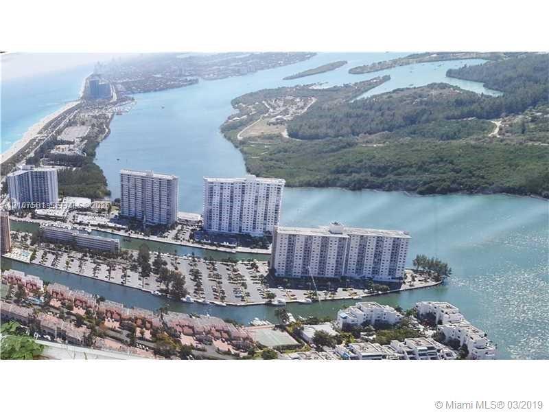 Aerial perspective featuring multiple high-rise buildings, extensive parking areas, water features, and surrounding natural landscapes