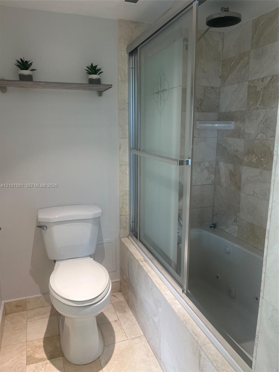 Tiled flooring with a built-in jetted tub, wall-mounted showerhead, and sliding glass shower enclosure