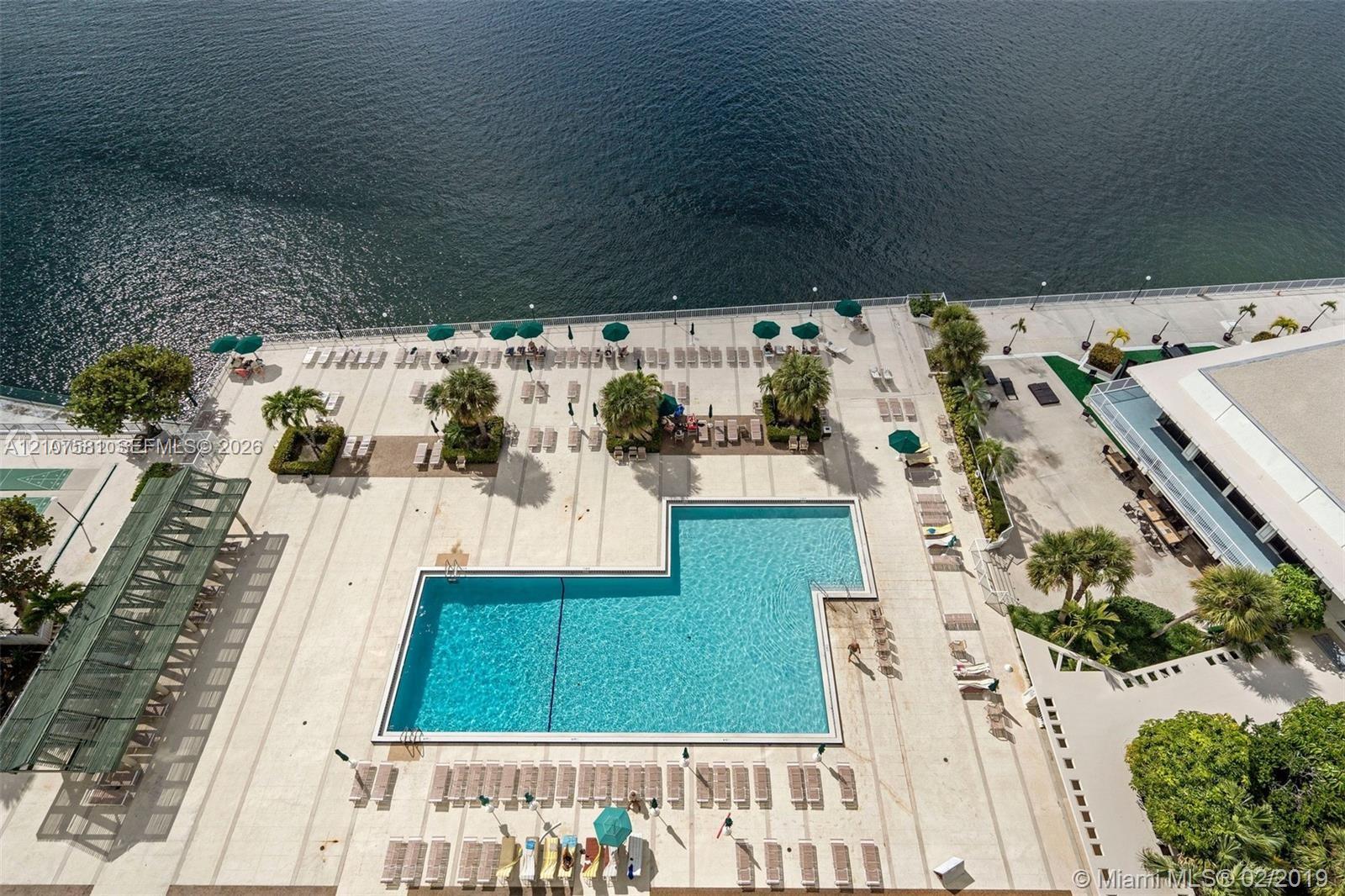Expansive waterfront pool deck featuring a geometric swimming pool, extensive lounge seating, and mature landscaping