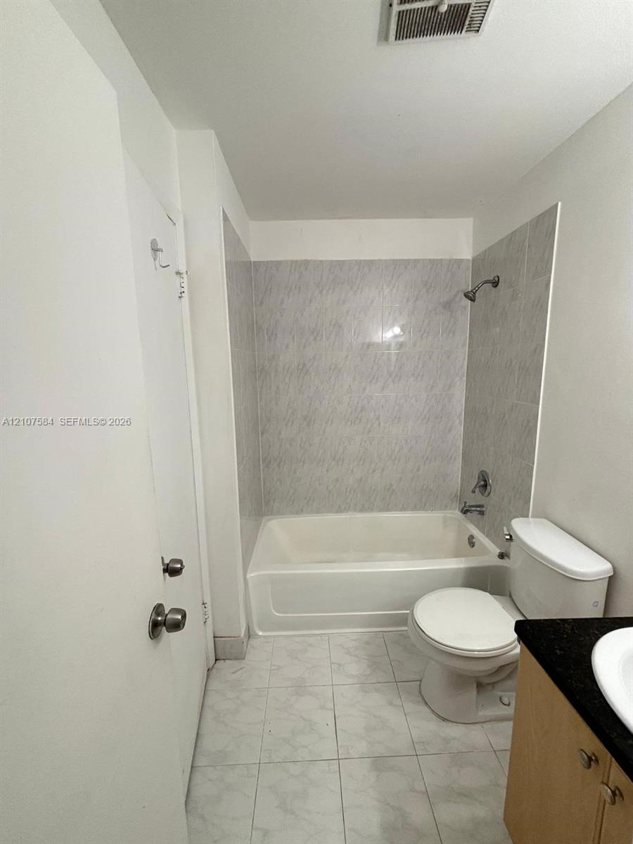 Full bathroom featuring a tub-shower combination with floor-to-ceiling tile surround, light-toned cabinetry, dark stone-finish countertop, and neutral tile flooring