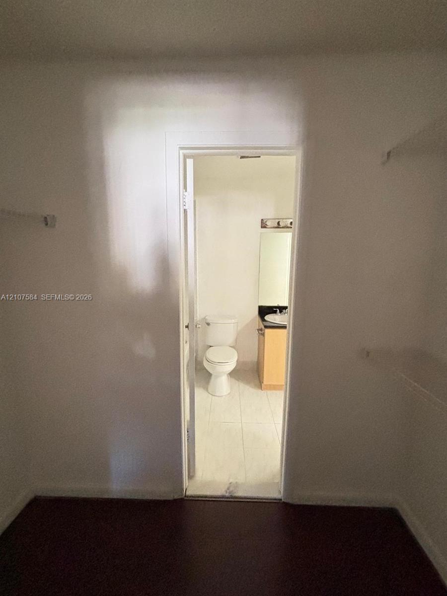 Storage area featuring built-in shelving, providing entry to a bathroom equipped with a vanity, countertop-integrated basin, and standard toilet