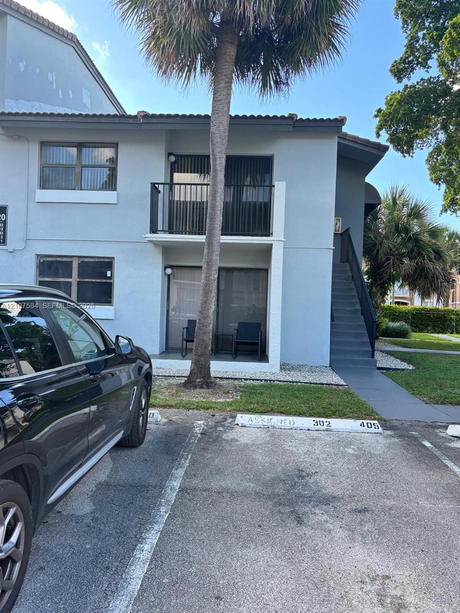 Two-story exterior featuring a private balcony, ground-level patio, exterior staircase, and assigned parking spaces