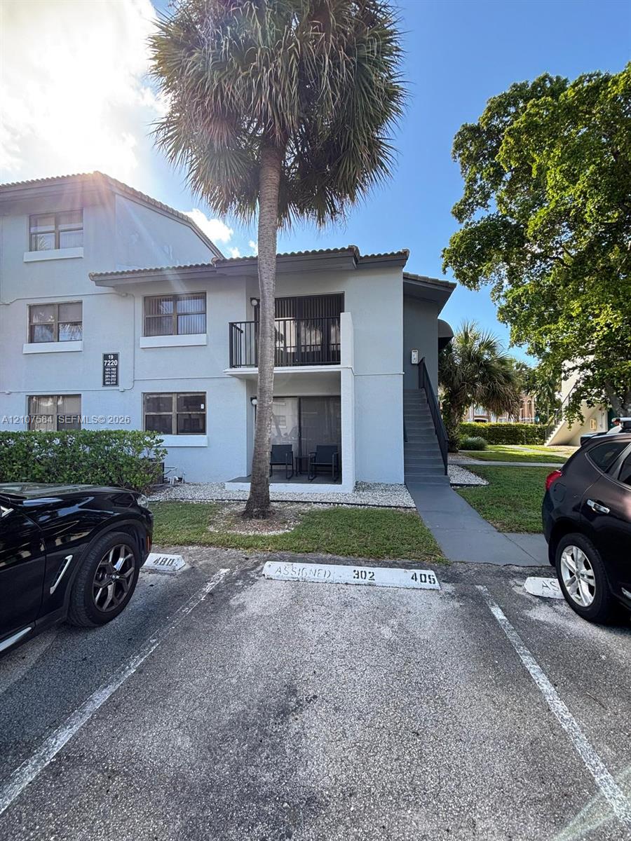 Exterior facade featuring stucco siding, a private balcony with metal railing, and dedicated asphalt parking